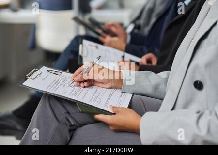 Nahaufnahme von Personen, die in einer Reihe sitzen und Dokumente für das Visum ausfüllen Stockfoto