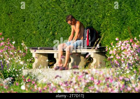 Ein Mann, der auf einer Bank in einem sonnigen Park sitzt Stockfoto