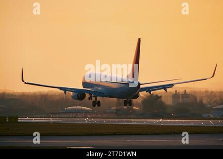 Flugzeug nähert sich der Landung auf der Start- und Landebahn des Flughafens. Passagierflugzeug im goldenen Licht des Sonnenuntergangs. Orangefarbener Himmel mit Kopierraum. Stockfoto