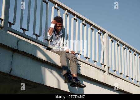 Afroamerikaner deprimierter Mann mit bandagierten Handgelenken, der auf der Brücke sitzt und an Selbstmord denkt Stockfoto