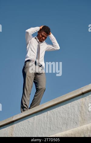 Vertikales Bild eines depressiven jungen Mannes, der Probleme hat, auf dem Dach zu stehen und Selbstmord zu begehen Stockfoto