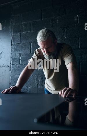 Vertikales Bild eines einsamen Mannes, der in einem dunklen Raum steht und über etwas nachdenkt Stockfoto