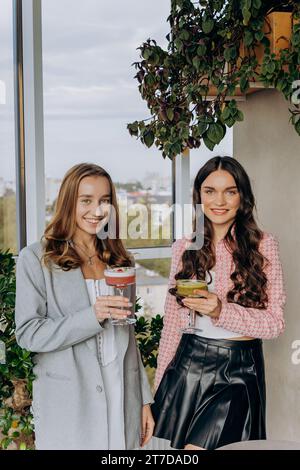 Attraktive Frauen stoßen im Restaurant oder in der Bar mit Cocktails an, während sie in die Kamera schauen Stockfoto