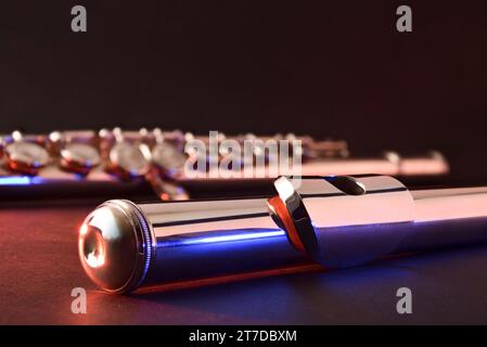 Detail des Flötenkopfes und des Körpers aus Metall im Hintergrund auf schwarzem Tisch mit roten und blauen Lichtern und dunklem isoliertem Hintergrund. Vorderansicht. Stockfoto