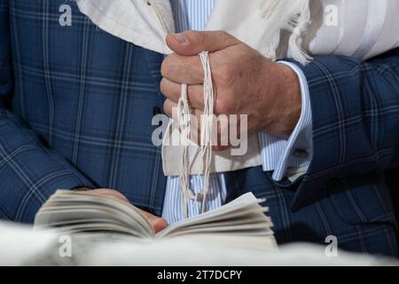 Nahaufnahme eines jüdischen Mannes, der betet, während er die Saiten oder Zitzit auf seinem Tallit in der Hand hält und das Schema jisrael-Gebet rezitiert. Stockfoto