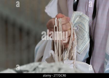 Nahaufnahme eines jüdischen Mannes, der betet, während er die Saiten oder Zitzit auf seinem Tallit in der Hand hält und das Schema jisrael-Gebet rezitiert. Stockfoto