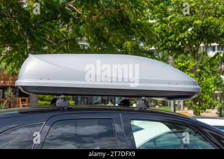 Schwarzer Kunststoff-Cargo auf dem Dach oder Dachträger für unterwegs. Abnehmbarer Aufbewahrungsbehälter, montiert auf dem Dachträger des Autos. Stockfoto