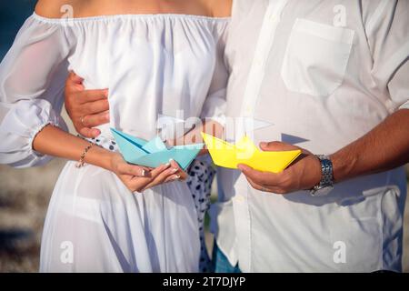 Mann- und Frauenhände mit blauen und gelben Papierbooten Stockfoto