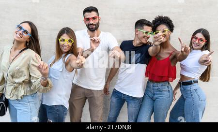 Eine vielfältige Gruppe junger Erwachsener trägt eine lebhafte Partybrille und teilt einen lustigen Moment auf einer Straße der Stadt. Stockfoto