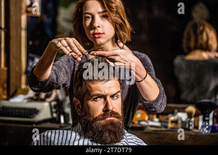 Arbeitende Haarschere. Professionelles Friseurmädchen schneidet Haare eines bärtigen Mannes. Er wird im Friseurladen frisiert. Friseur, Schönheitssalon. Bartmann Stockfoto