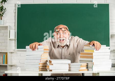 Portrait männlicher Lehrer im Klassenzimmer. Der lustige Lehrer hat viele Bücher in der Schule. Lehrer mit Büchern in der Schule. Mann Grundschullehrer steht da Stockfoto