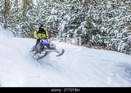 Schneemobil bewegt sich im Winterwald in den Bergen. Mann und schnelle Action-Schneemobil-Springen. Springen auf einem Schneemobil vor dem Hintergrund des Winters Stockfoto