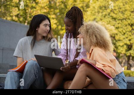 Drei multiethnische Studenten diskutieren nach dem Unterricht gemeinsam über die Notizen, die sie gemacht haben, und bereiten die nächste Prüfung vor Stockfoto