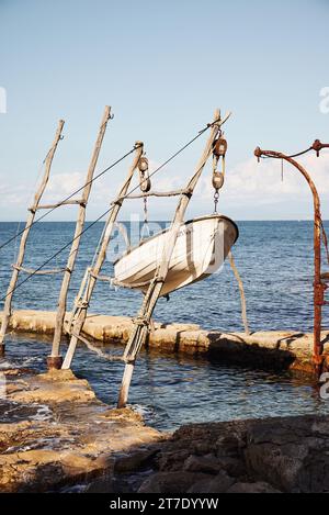 Ein leeres Holzboot in einem heruntergekommenen Steg am Wasserrand, mit einem wolkigen Blau darüber Stockfoto