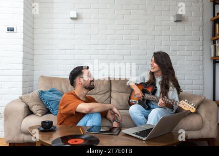 Junges kreatives Paar, freiberufliche Webdesigner, die eine Pause machen und Spaß beim Spielen von E-Gitarren haben, Musik in ihrer Home Office-Liste zu hören Stockfoto