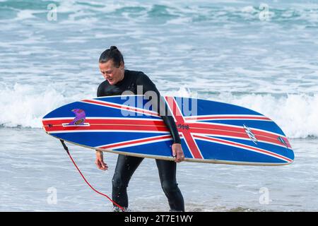 Ein müder Surfer mit einem unverwechselbaren Surfbrett nach einer Surfsession in Fistral in Newquay in Cornwall in Großbritannien. Stockfoto