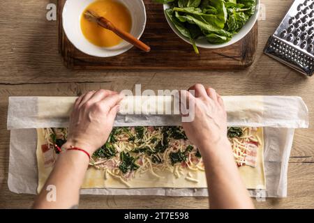 Der Koch rollt Blätterteig mit Speck, Spinat und Käse, bereitet Mini-Pizzakuchen zu - Top of View. Rezeptverfahren: 5 von 10 Stockfoto