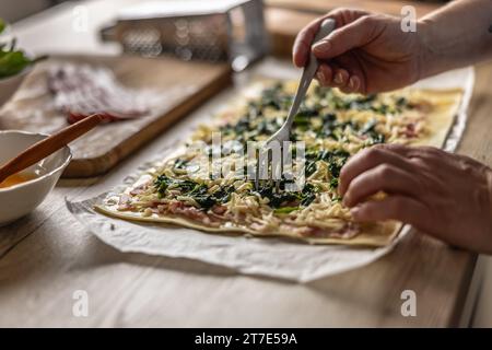 Der Koch bereitet Mini-Pizzakuchen zu, gibt Spinat auf Blätterteig mit Käse und Speck. Rezeptverfahren: 4 von 10 Stockfoto