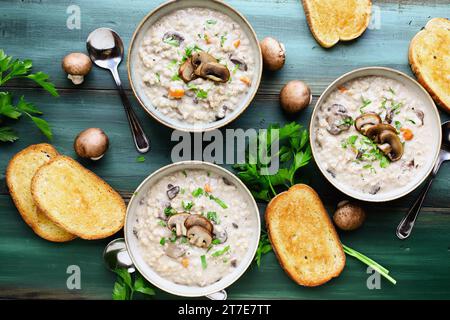 Drei Schüsseln Pilzsuppe mit Portabella-Pilzen, Karotten und frischer Petersilie. Serviert mit geröstetem französischem Brot auf einem grünen Holztisch. Gemeinkosten. Stockfoto