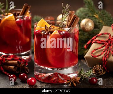 Glühwein mit Preiselbeeren, Orangenscheiben, Zimt, Rosmarin und Anis. Weihnachtsdekoration im Hintergrund Stockfoto