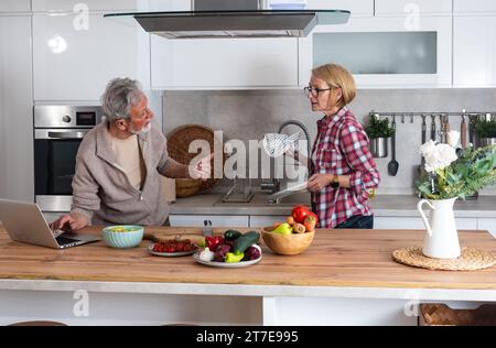 Seniorenpaar kochen gemeinsam in der Küche zum goldenen Hochzeitstag und lesen Rezepte aus dem Internet auf Laptop. Ältere Männer und Frauen machen sich gut Stockfoto