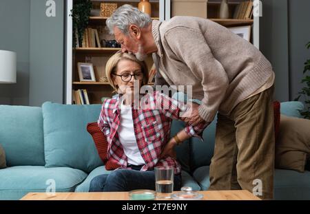 Älteres Paar älterer Mann, Mann, der aufpasst, ihre kranke Frau tröstet, massiert sie und umarmt sie, weil sie jahrelang Schmerzen und Kopfschmerzen hat Stockfoto