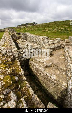 Die Ruinen der öffentlichen römischen Latrinen im Housesteads Fort entlang der Hadrian’s Wall im Norden Großbritanniens, mit Sturmwolken im Hintergrund Stockfoto