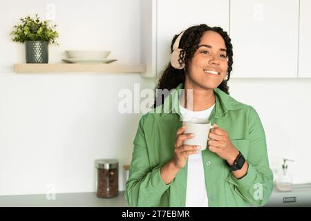 Glückliche Afroamerikanische Dame, Die Kopfhörer Trägt Und Drinnen Einen Kaffeetasse Hält Stockfoto