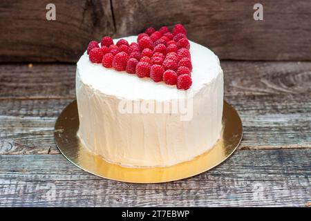 Eleganter weißer Kuchen mit Himbeerherz für St. Valentinstag, Muttertag oder Geburtstag, dekoriert mit frischem Beerenzucker auf hölzernem Hintergrund Stockfoto