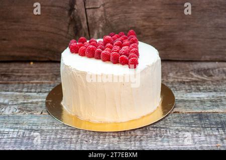 Eleganter weißer Kuchen mit Himbeerherz für St. Valentinstag, Muttertag oder Geburtstag, dekoriert mit frischem Beerenzucker auf hölzernem Hintergrund Stockfoto