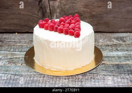 Eleganter weißer Kuchen mit Himbeerherz für St. Valentinstag, Muttertag oder Geburtstag, dekoriert mit frischem Beerenzucker auf hölzernem Hintergrund Stockfoto