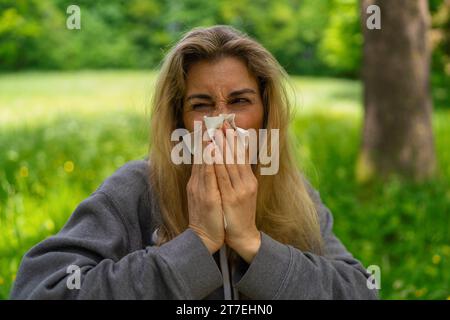 Frau, die ihre Nase mit Gewebe im Park beim Sping bläst, wegen einer Allergie gegen Pollen Stockfoto