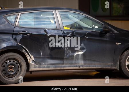 Das Fahrzeug wird von der Seite gesehen. Delle am Fahrzeug. Kratzer in Fahrzeugen. Details der Unfallschäden. Schwarzer Transport. Stockfoto