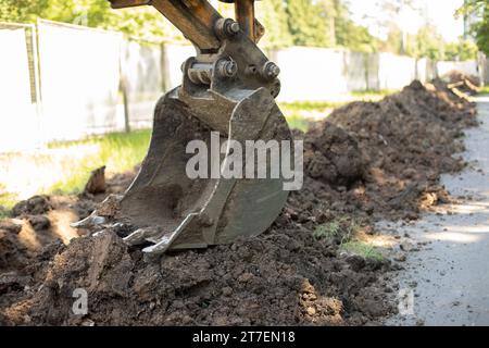 Rolltreppeneimer gräbt Boden. Schwere Maschinen auf der Baustelle. Verlegen von Rohren im Boden. Stahlkübel zum Anheben des Bodens. Stockfoto