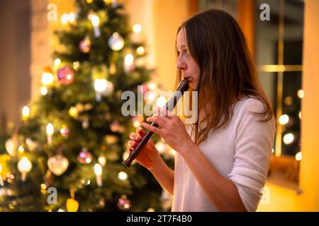 15.11.2023, Weihnachten 2023 in Deutschland, ein festlich dekorierter Weihnachtsbaum in einer Wohnung im Unterallgäu. Eine Frau spielt Blockflöte im Wohnzimmer am Heiligen Abend. Modellveröffentlichtes 15.11.2023, Weihnachtsbaum 15.11.2023, Weihnachtsbaum *** 15 11 2023, Weihnachten 2023 in Deutschland, Ein festlich geschmückter Weihnachtsbaum in einer Wohnung im Unterallgäu spielt Eine Frau am Heiligabend im Wohnzimmer Blockflöte Modellveröffentlichtes 15 11 2023, Weihnachtsbaum 15 11 2023, Weihnachtsbaum Credit: Imago/Alamy Live News Stockfoto