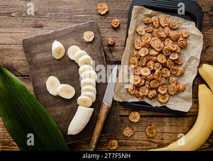 Frische rohe Bananenscheiben mit getrockneten Bananenchips auf hölzernem Hintergrund mit grünem Blatt. Stockfoto