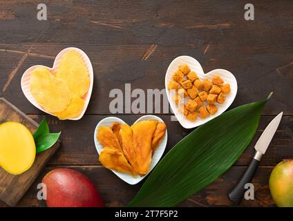 Getrocknete Mangoblätter und -Kugeln in herzförmigen Platten auf hölzernem Hintergrund. Ansicht von oben. Stockfoto