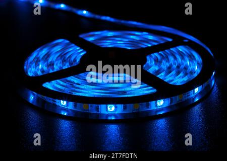 Eine Rolle mit LED-Streifen mit leuchtend neonblauen Lampen auf dem Tisch in einem dunklen Raum Stockfoto