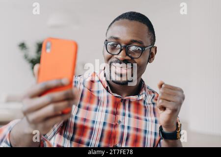 Ein Mann mit Brille teilt aufgeregt Inhalte auf seinem Smartphone und feiert den Erfolg Stockfoto