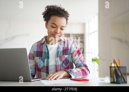 Fokussiertes Black Girl studiert mit Laptop und Notizen in einem hellen Zuhause Stockfoto