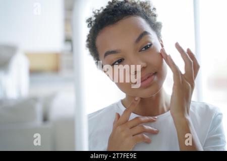 Die sanfte schwarze Frau berührt ihr Gesicht und betrachtet Schönheit im natürlichen Licht Stockfoto