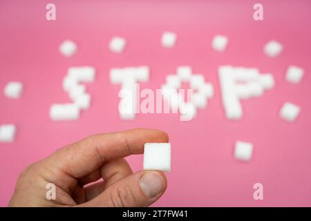 Augsburg, Bayern, Deutschland - 15. November 2023: Hand mit einem Stück Zucker vor dem Zuckerbuchstaben Stop. Ungesundes Zuckerkonsum-Konzept *** Hand hält ein Stück Würfelzucker vor den Zucker Schriftzug Stop. Ungesunder Zuckerkonsum Konzept Credit: Imago/Alamy Live News Stockfoto