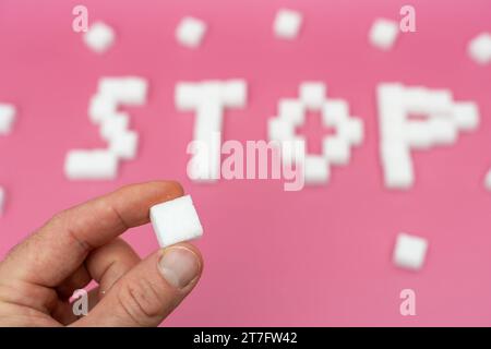 Augsburg, Bayern, Deutschland - 15. November 2023: Hand mit einem Stück Zucker vor dem Zuckerbuchstaben Stop. Ungesundes Zuckerkonsum-Konzept *** Hand hält ein Stück Würfelzucker vor den Zucker Schriftzug Stop. Ungesunder Zuckerkonsum Konzept Credit: Imago/Alamy Live News Stockfoto