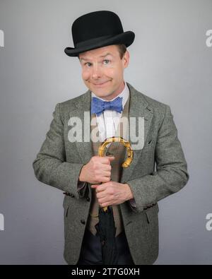 Britischer Charakter im Tweed-Anzug und Bowler-Hut, der einen Regenschirm hält und lächelnd ist. Konzept des Vintage Vaudeville Comic Schauspielers Stockfoto