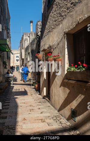 Eine enge Gasse im mittelalterlichen Dorf mit den typischen Steinhäusern und Wanderern im Frühling, Borgio Verezzi, Savona, Ligurien, Italien Stockfoto