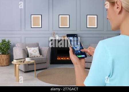 Frau, die Smart Home Control System über Anwendung auf Handy in Innenräumen, Nahaufnahme Stockfoto