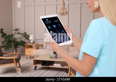 Frau mit Smart Home Control System über Anwendung auf Tablet in Innenräumen, Nahaufnahme Stockfoto