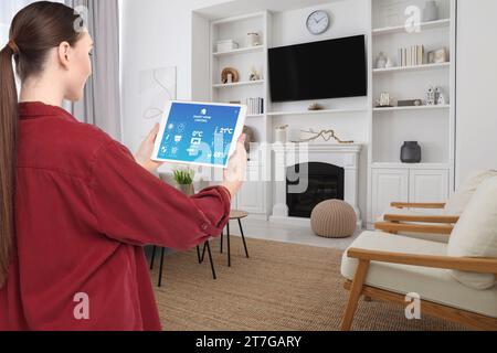 Frau, die das Smart Home Control System über Anwendung auf Tablet in Innenräumen verwendet Stockfoto