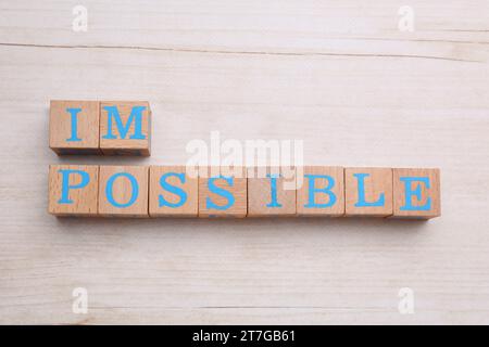 Motivationskonzept. Wortwechsel vom Unmöglichen in möglich durch Entfernen von Würfeln auf hellem Holztisch, flacher Lay Stockfoto