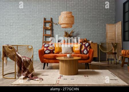 Stilvolles Wohnzimmer mit orangefarbenem Sofa, modernem Sessel und hölzernem Couchtisch Stockfoto